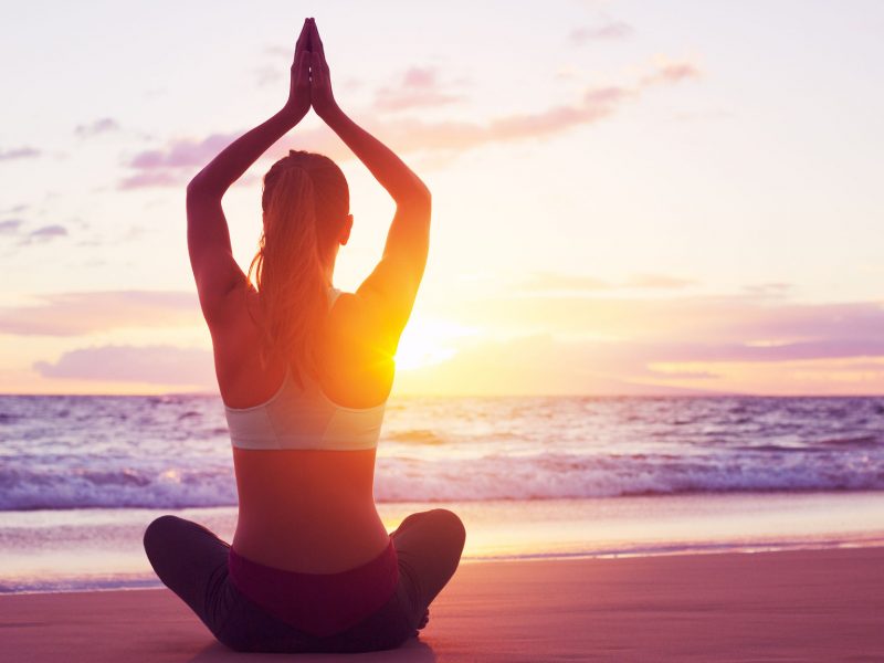 Young healthy woman practicing yoga on the beach at sunset